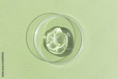 Hyaluronic acid serum or gel for the face in Petri dish on a green background. Concept of cosmetics laboratory researches, wellness and beauty. Cosmetic texture. Top view.