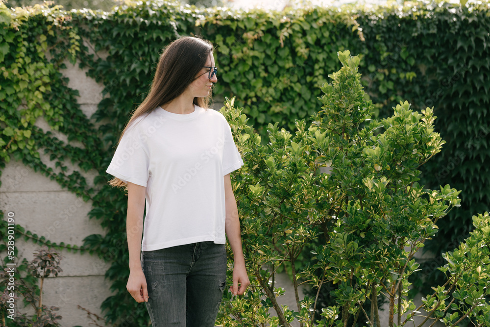 Woman wearing white t-shirt with space for logo or design in the park in summer Woman wearing white t-shirt with space for logo or design in the park in summer