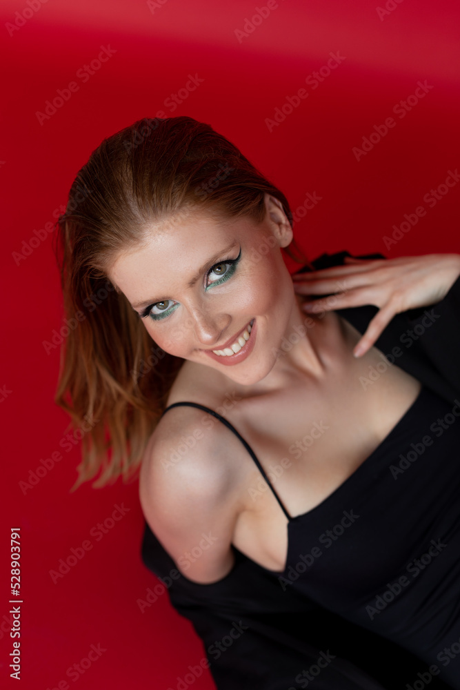 Vertical smiling blonde woman in black dress and capote look camera and posing in red studio. Mascara, eyeliner, shades Vertical smiling blonde woman in black dress and capote look camera and posing in red studio. Mascara, eyeliner, shades