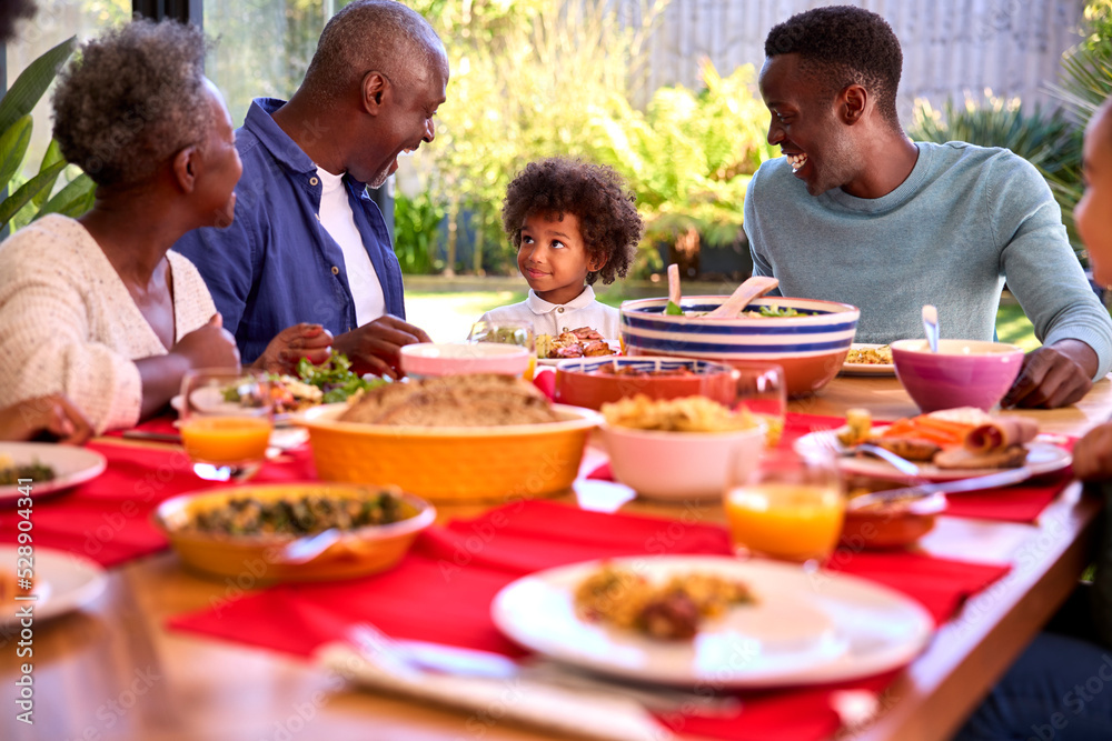 Multi-Generation Family Sitting Around Table At Home Enjoying Meal Together Multi-Generation Family Sitting Around Table At Home Enjoying Meal Together