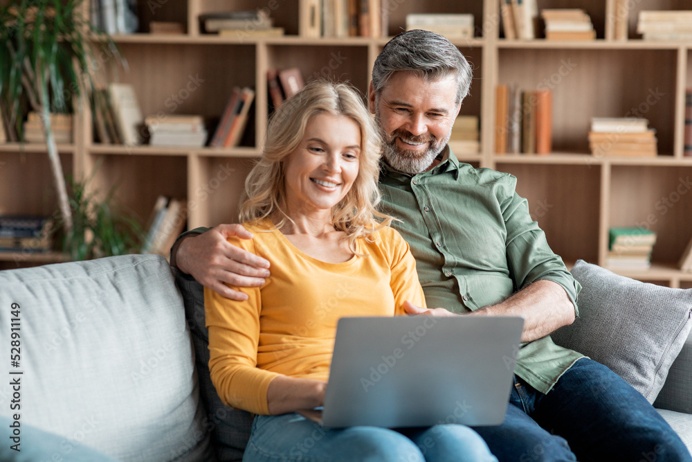 Smiling Middle Aged Spouses Resting With Laptop In Living Room Interior