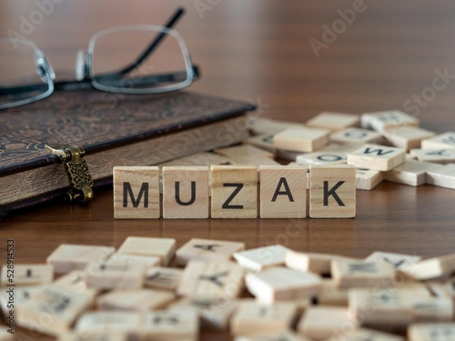 muzak word or concept represented by wooden letter tiles on a wooden table with glasses and a book