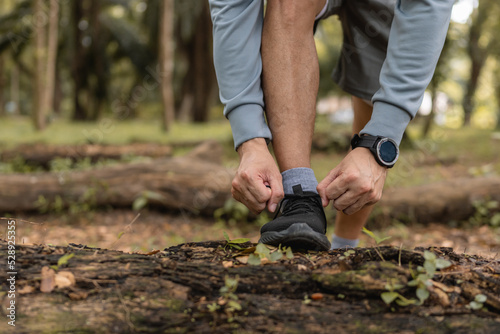 Man tying running shoes on path forest, preparing for a run exercise workout outdoor.
