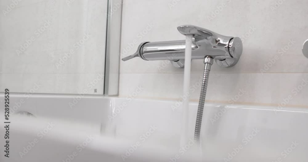 Hand opening and closing a shiny metal bathtub faucet in a luxurious bathroom Hand opening and closing a shiny metal bathtub faucet in a luxurious bathroom