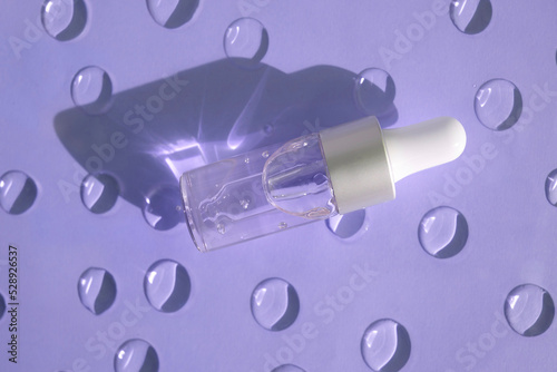 A bottle of a cosmetic product with bubbles casts a shadow on a blue background with gel drops.