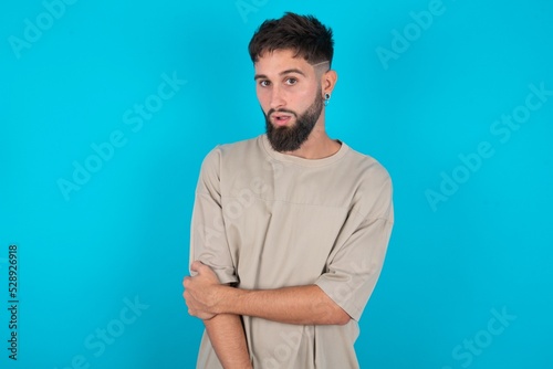 Shocked embarrassed bearded caucasian man wearing casual T-shirt over blue background keeps mouth widely opened. Hears unbelievable novelty stares in stupor