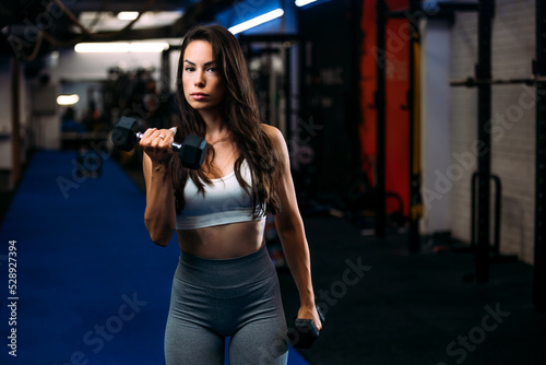 Young fit beautiful woman doing exercises with dumbbell in fitness club.