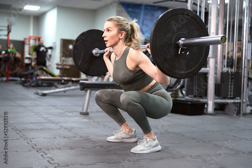 Front view of caucasian woman lifting heavy barbell in the gym