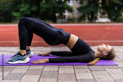 Fit young woman training on mat outdoor summer day, performing reverse plank stretching spinal muscles, doing fascia exercise. Warm-up before workouts routine, health care