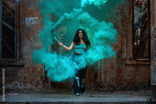 Young girl posing with turquoise smoke in an abandoned place
