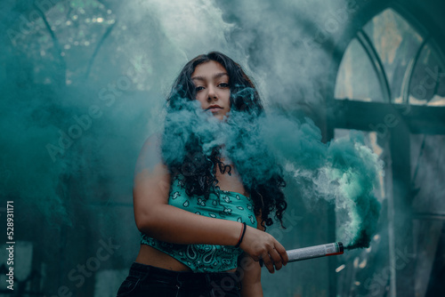 Young girl posing with turquoise smoke in an abandoned place