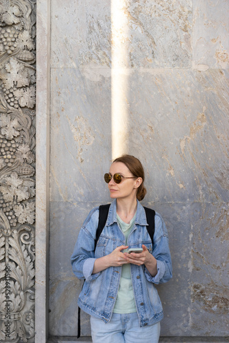 Woman next to stands behind a granite wall, free space for copy of text, waiting for meeting and date, smartphone in hand, online message, communication on phone.