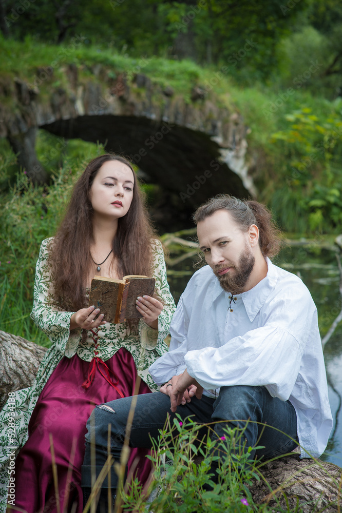 Obraz premium Beautiful young woman in medieval style dress reading book for handsome man sitting on the tree