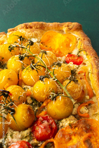 Homemade pie made of puff pastry and yellow, orange and red tomatoes, savory square pie on a green background, top view, copy space