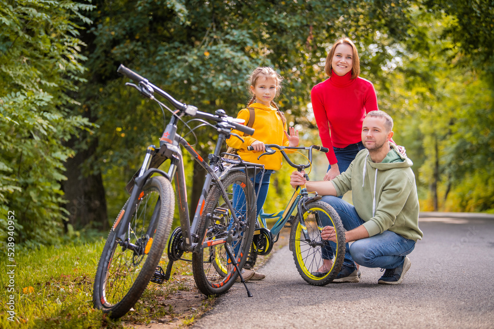 Dad, mom and daughter walk with their bicycles along autumn path of the park. Dad, mom and daughter walk with their bicycles along autumn path of the park.