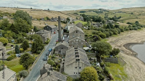 Aerial video footage of a rural industrial village with old mill and chimney stack. Shot at Leeming above Oxenhope and adjacent to Leeming Reservoir. Shot in West Yorkshire England. photo