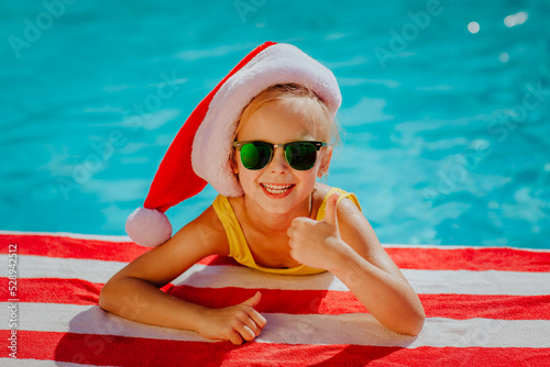Girl with Christmas cap posing near the swimming pool on stripped towel.