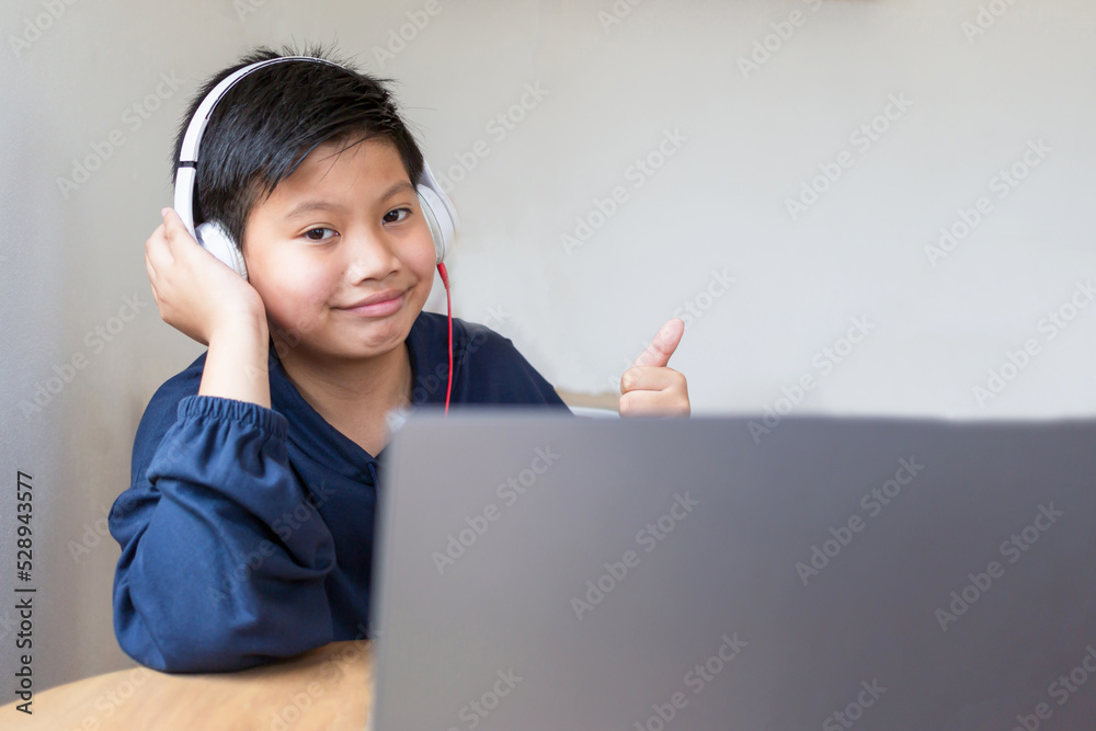 Asian boy cute boy wears headphones showing thumbs up and smiling while looking into the camera After studying online with laptop computer at home. Asian boy cute boy wears headphones showing thumbs up and smiling while looking into the camera After studying online with laptop computer at home.