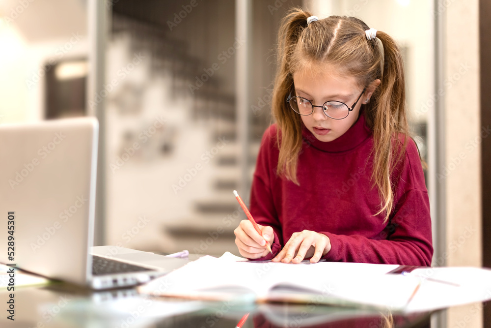 Cute student little girl seriously doing homework using laptop at home. Kids distance learning. Online education concept Cute student little girl seriously doing homework using laptop at home. Kids distance learning. Online education concept