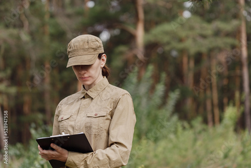 A woman biologist in uniform with a clipboard explore the forest biocenosis in national park in summer, selective focus. photo