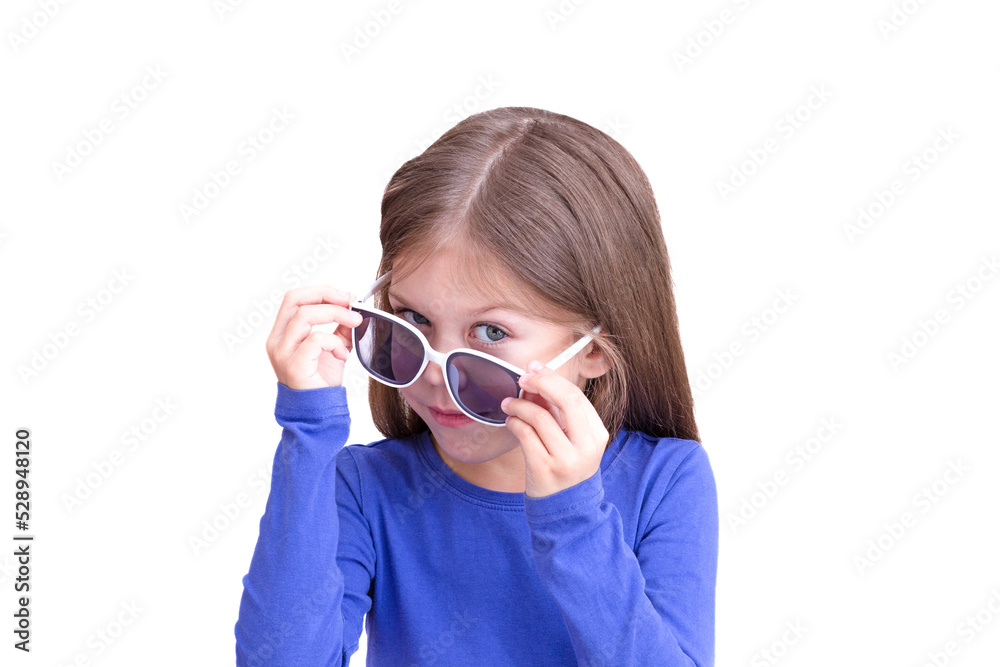 Smiling child holding white sunglasses down on eyes and look out, isolated on white background looking at camera waist up caucasian little girl of 5 years in blue