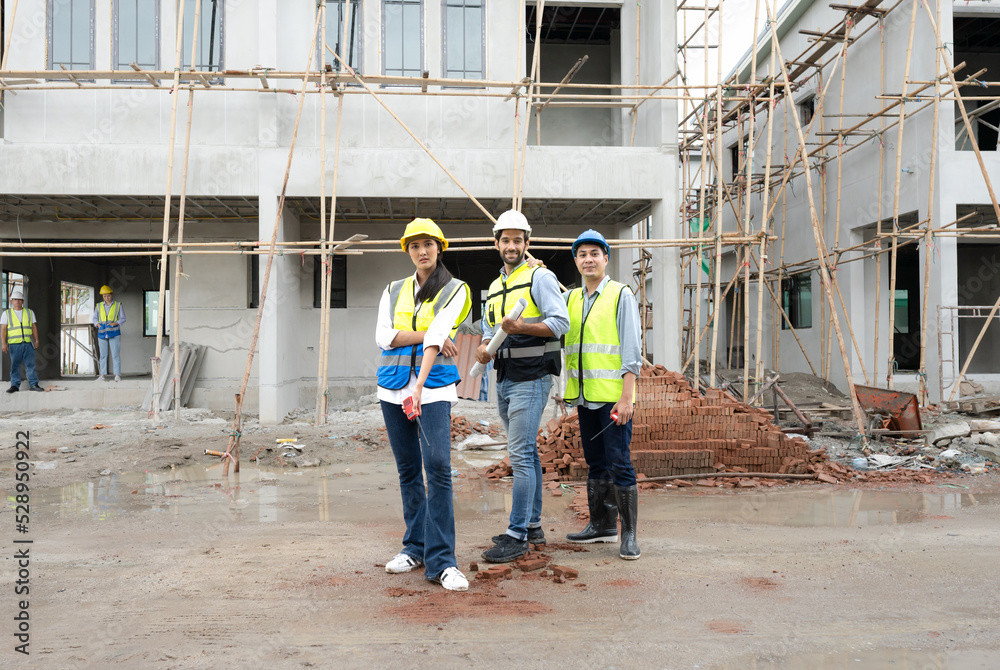 Construction engineer and architect team discuss housing development project at construction site. Contractor manager inspecting residential building estate infrastructure. Men, woman at work outdoor.