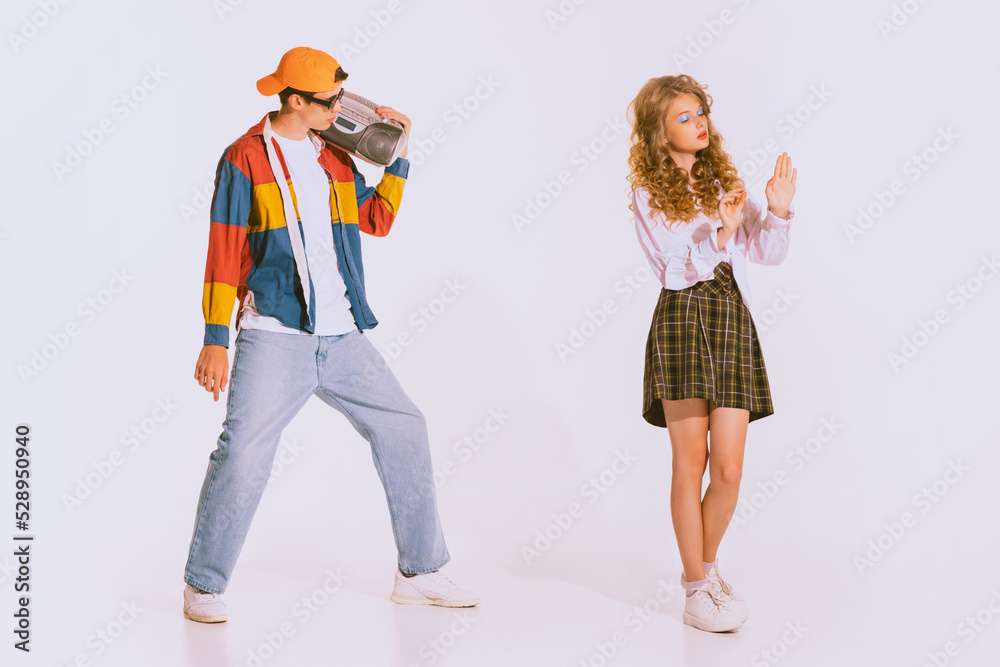 Portrait of stylish young man in trendy colorful jacket with music player posing with beautiful girl isolated over grey background
