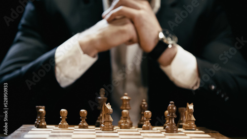Cropped view of blurred businessman near chess board isolated on black.