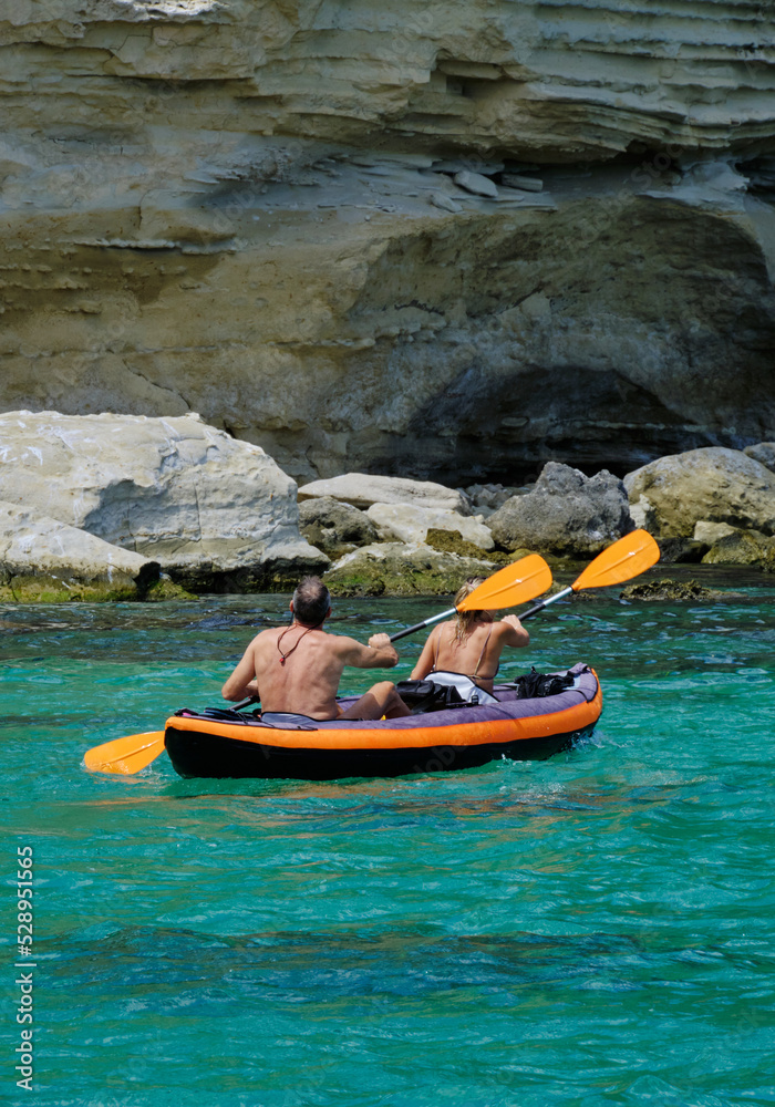 woman and man riding kayaks at sea bay between big rocks.