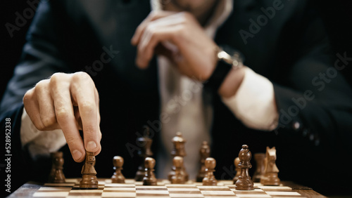 Cropped view of blurred businessman holding chess figure isolated on black.