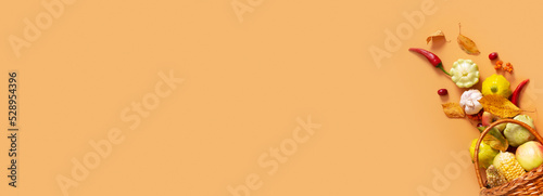 Autumn banner with harvest basket with corn, apples, zucchini and peppers on a orange background with copy space