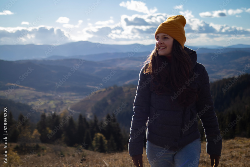 Young happy woman in orange beanie is walking in front of mountains landscape