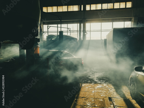 Abstract soft image of a dark room of a car workshop. A thick veil of smoke hangs in the air. The sun's rays through the windows illuminate the silhouettes of cars. Cinematic image.