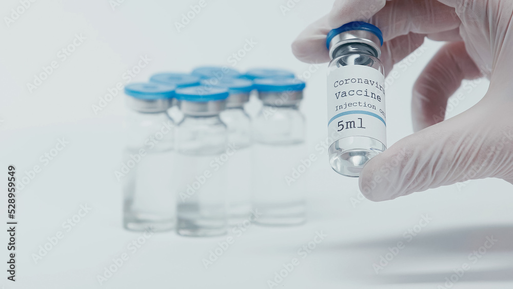 cropped view of person taking bottle with coronavirus vaccine liquid on white.