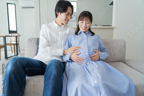 自宅で笑顔でお腹をさする日本人夫婦