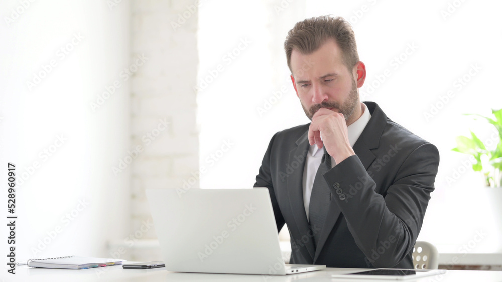 Young Businessman Thinking while Working on Laptop in Office Young Businessman Thinking while Working on Laptop in Office