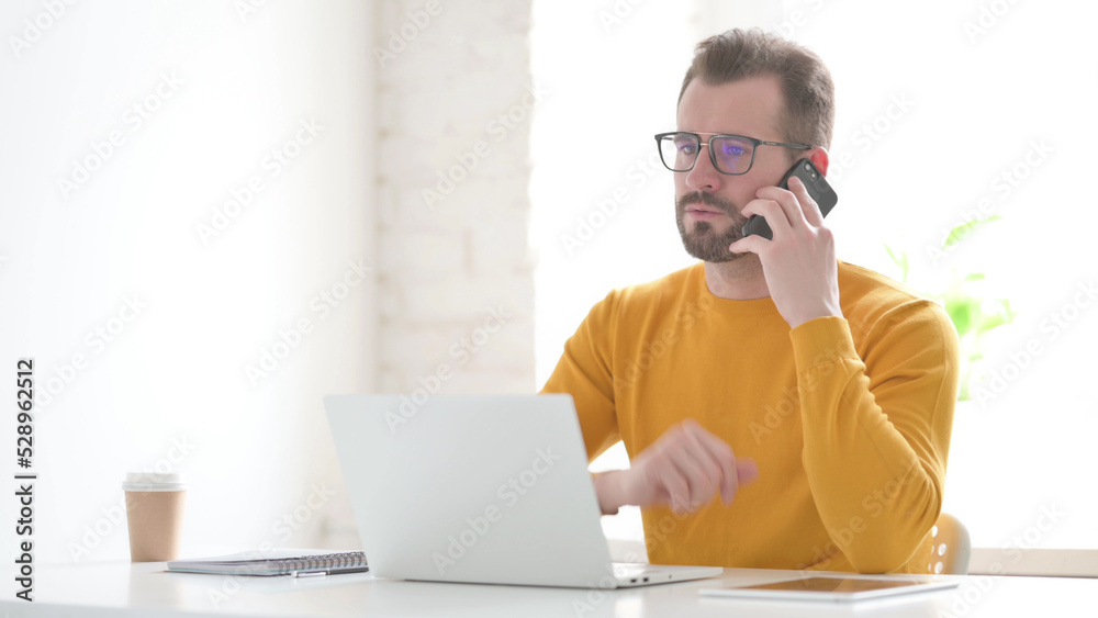 Man Talking on Phone while using Laptop in Office Man Talking on Phone while using Laptop in Office
