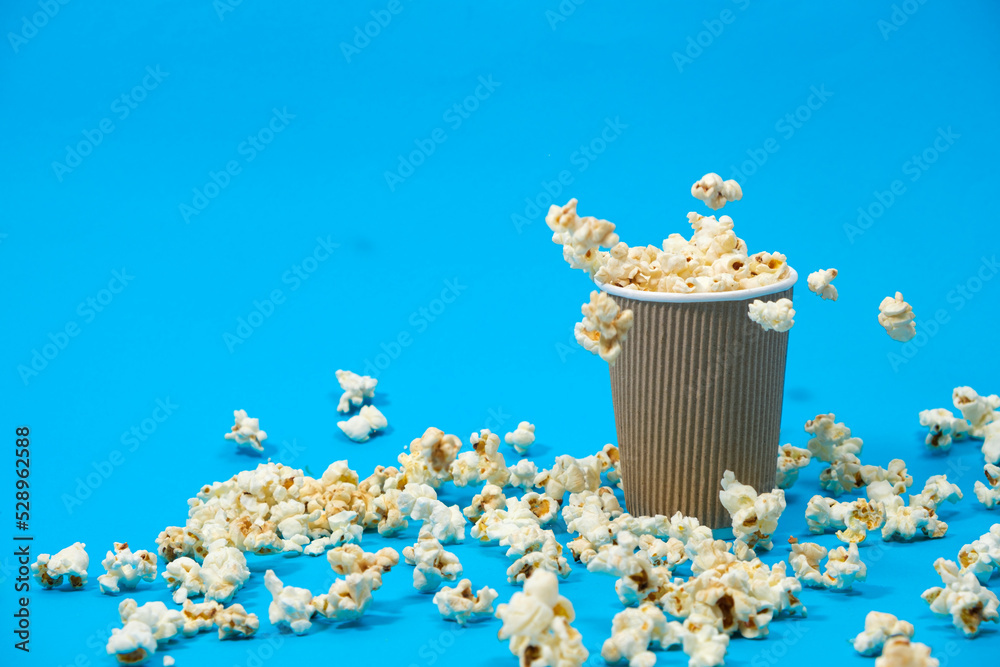 Popcorn is poured into a paper brown glass on a blue background with place for text.
