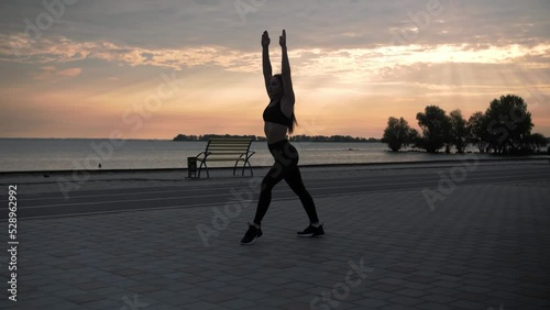 Young woman doing backflips.Girl doing acrobatic activity against the sea at sunrise. Fitness Lifestyle slow motion.