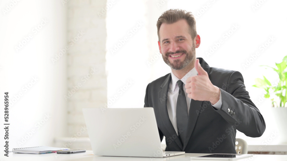 Young Businessman Showing Thumbs Up Sign While using Laptop in Office Young Businessman Showing Thumbs Up Sign While using Laptop in Office