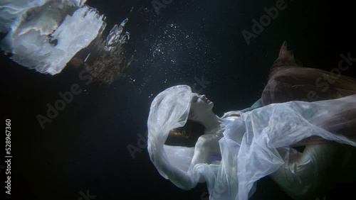 a red-haired woman hovers with a translucent cloth in dark water and is reflected in the surface. the camera is tilted. the general plan