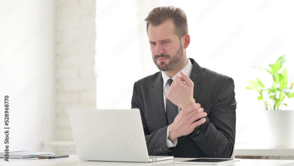 Young Businessman having Wrist Pain while using Laptop in Office Young Businessman having Wrist Pain while using Laptop in Office