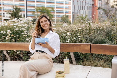 фотографія Happy young caucasian girl eats homemade food taken in bowl sitting on bench