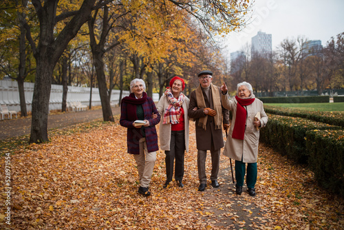 Group of happy senior friends with books on walk outdoors in park in autumn, talking and laughing photo