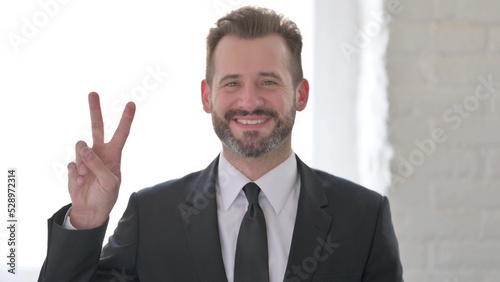 Middle Aged Businessman showing Victory Sign with Finger