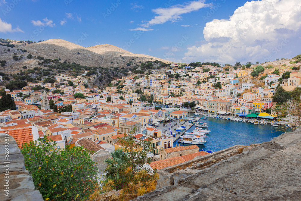 Panoramic view, aerial skyline of small haven of Symi island. Village with tiny beach and colorful houses located on rock. Tops of mountains on Rhodes coast, Dodecanese, Greece . High quality photo