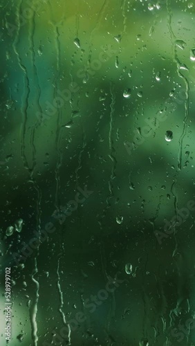 Vertical video. Stormy rainy weather behind the window, close up of rain drops streaming slowly, nature and severe weather concept