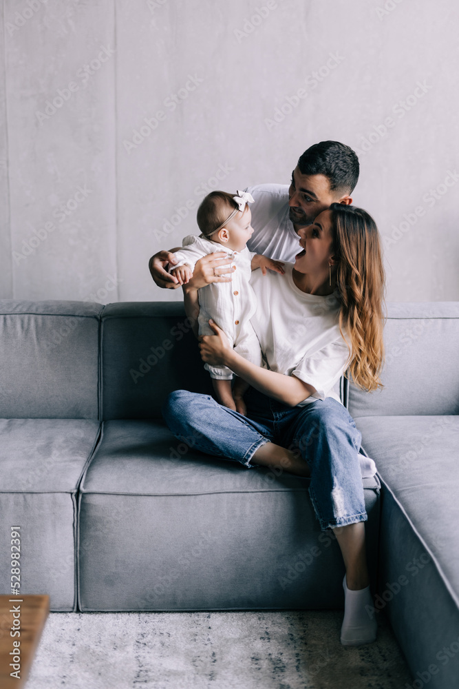 Naklejka premium Proud mother and father smiling at newborn baby daughter, sitting on the sofa at home