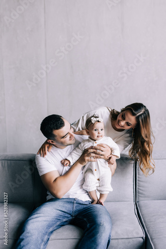 Proud mother and father smiling at newborn baby daughter, sitting on the sofa at home