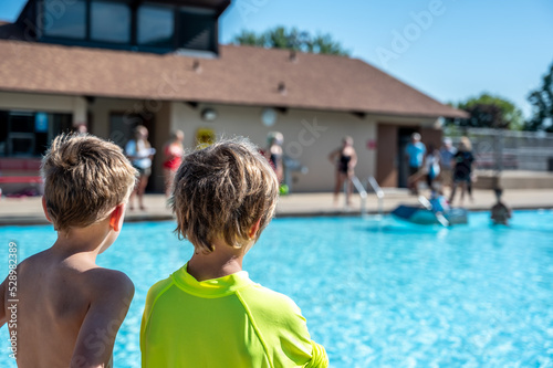 Two boys looking towards a cardboard boat floating in a pool.